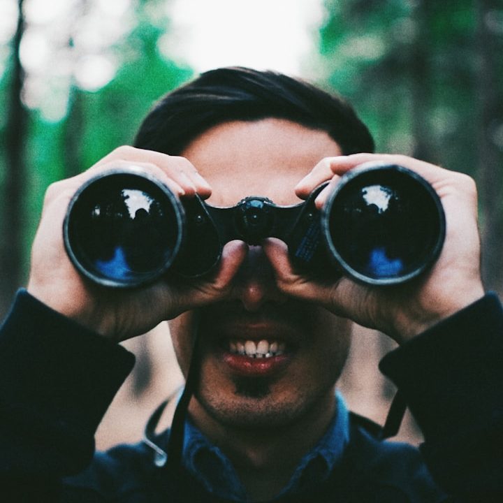 Mann mit Fernglas in der Natur, lächelt in die Kamera.